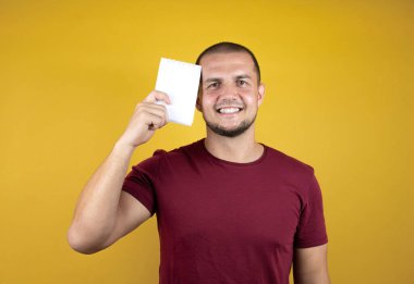 Rus adam, sarı tişörtlü, izole edilmiş arka planda gülümseyen ve elinde boş bir not defteri olan sıradan bir kırmızı tişört giyiyor.
