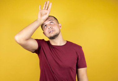 Rus adam sarı lekeli arka planda kırmızı tişört giyiyor. Alnına dokunuyor. Hastalık, ateş, grip, soğuk algınlığı, virüs...