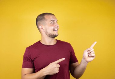 Rus adam sarı arkaplan üzerine kırmızı tişört giyip gülümsüyor ve iki parmağıyla gülümsüyor.