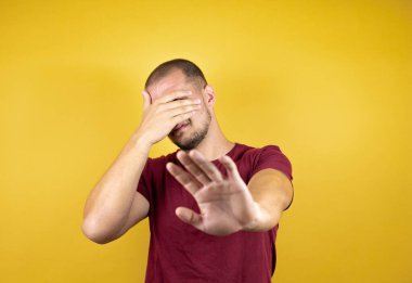 Rus adam sarı tişörtü giyip elleri ile izole edilmiş arka plan ve üzgün ve korku ifadesiyle jestleri durduruyor. Utanç verici ve olumsuz bir kavram..
