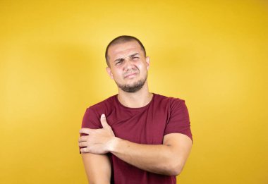 Rus adam sarı arka plan üzerine kırmızı tişört giyiyor. Omzunda ağrı ve acı dolu bir ifade var.