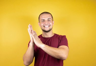 Rus adam, sarı arka plan üzerine kırmızı tişört giyip mutlu ve mutlu, gururlu elleri alkışlıyor ve alkışlıyor.