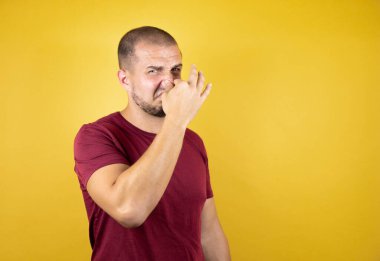 Rus adam sarı arkaplan üzerine kırmızı tişört giymiş pis ve iğrenç bir koku alıyor. Nefesini burnunda tutuyor.