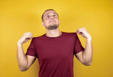 Rus adam sarı arkaplan üzerine kırmızı tişört giyiyor ve başarılı bir ifade takınıyor.