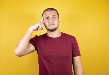 Rus adam, sarı arka plan üzerine kırmızı tişört giymişti. Bir elini kafasına koyup sanki bir şey unutmuş gibi gülümsüyordu.