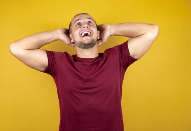 Rus adam, sarı tişört giyiyordu. İzole edilmiş arka plan, gevşeme ve esneme, kollar ve eller başının arkasında mutlu bir gülümseme.