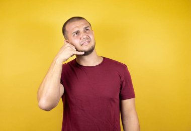 Sarı arkaplan üzerine kırmızı tişört giyen Rus bir adam telefonda el ve parmaklarıyla telefon hareketlerine şaşırdı. Telefonda konuşmak gibi.