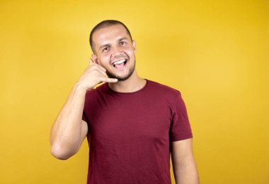 Rus adam, sarılı arka planda kırmızı tişört giyiyor. Gülümsüyor, el ve parmaklarıyla telefonla konuşuyor gibi.