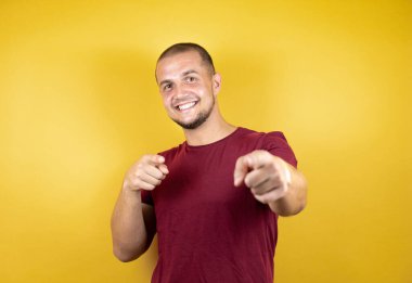 Sarı arka plan üzerine kırmızı tişört giyen Rus adam mutlu ve komik yüzlü parmaklarını kameraya doğrultuyor. İyi enerji ve titreşimler.