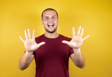 Rus adam, sarı tişörtlü, özgüvenle gülümseyen ve mutlu bir şekilde 10 numaralı parmaklarıyla işaret ediyor..