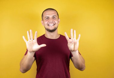 Rus adam sarı tişörtlü, özgüvenle gülümseyen ve mutlu bir şekilde dokuz numarayı işaret ediyor..