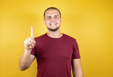 Rus adam, sarı tişörtlü, özgüvenle gülümseyen ve mutlu bir şekilde bir numaralı parmaklarıyla işaret ediyor..