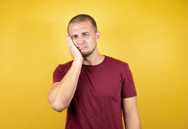 Rus adam sarı arkaplan üzerine kırmızı tişört giyip diş ağrısı ya da diş ağrısı yüzünden ağız ve acı dolu yüz ifadelerine dokunuyor.