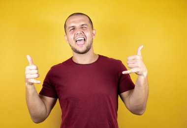 Rus adam sarı arkaplan üzerine kırmızı tişört giymiş çılgın bir ifadeyle bağırıyor elleri havada rock sembolü yapıyor.