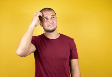 Rus adam, sarı arka plan üzerine kırmızı tişört giymişti. Bir elini kafasına koyup sanki bir şey unutmuş gibi gülümsüyordu.