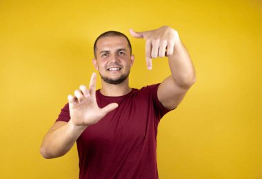 Rus adam, sarı arkaplan üzerine kırmızı tişört giymiş. El ve parmakları kullanarak çerçeve yapıyor. Kamera perspektifi.