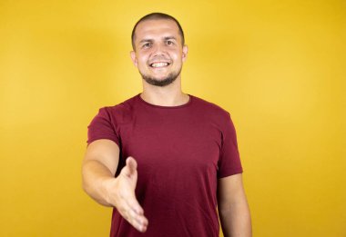 Rus adam, sarı tişörtlü, özensiz, tebessümlü, dostça bir selamlama ve hoş geldin hediyesi olarak kırmızı tişörtü giyiyor.