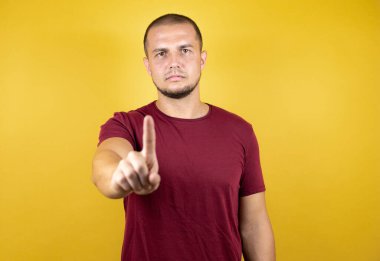Rus adam sarı tişörtlü ve sarı izole edilmiş arka planda bir numaralı parmaklarıyla işaret ederken ciddi.