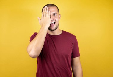 Rus adam, sarı tişörtlü, titiz kırmızı tişörtlü. İzole edilmiş arka plan. Bir gözünü elinle kapatıyor..