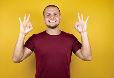 Rus adam sarı izole arkaplan üzerine kırmızı tişört giymiş, gülümsüyor ve iki eliyle ve parmaklarıyla 