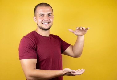 Rus adam, sarı tişörtlü, eskimiş arka planda büyük ve büyük boyut işareti gösteren işaretlerle şaşırmış ve el kol hareketi yapmış. Ölçü sembolü.