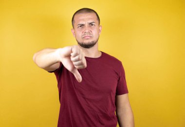 Rus adam sarı izole arkaplan üzerine kırmızı tişört giymiş mutsuz, kızgın, reddedilmiş ve olumsuz jestler yapıyor. Kötü ifade