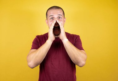 Rus adam sarı arka plan üzerine kırmızı tişört giyip el ele bağırıyor ve bağırıyordu. İletişim konsepti.