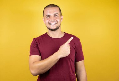 Rus adam, sarı tişört giyiyordu. İzole edilmiş arka plan, gülümsüyordu ve başparmağıyla yan tarafı gösteriyordu..