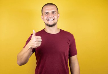 Rus adam sarı izole arkaplan üzerine kırmızı tişört giyerek mutlu bir el hareketi yapıyor. Kameraya bakıp başarıyı gösteren ifade onaylanıyor