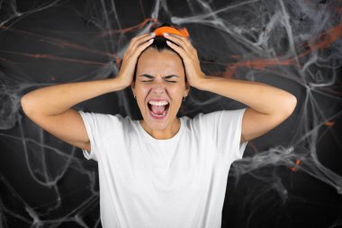 Siyah arka planda, baş ağrısı çeken örümcek ağları ve örümcekleri olan genç ve güzel bir kadın. Umutsuz ve stresli, çünkü elleri başının üstünde acı ve migren var.