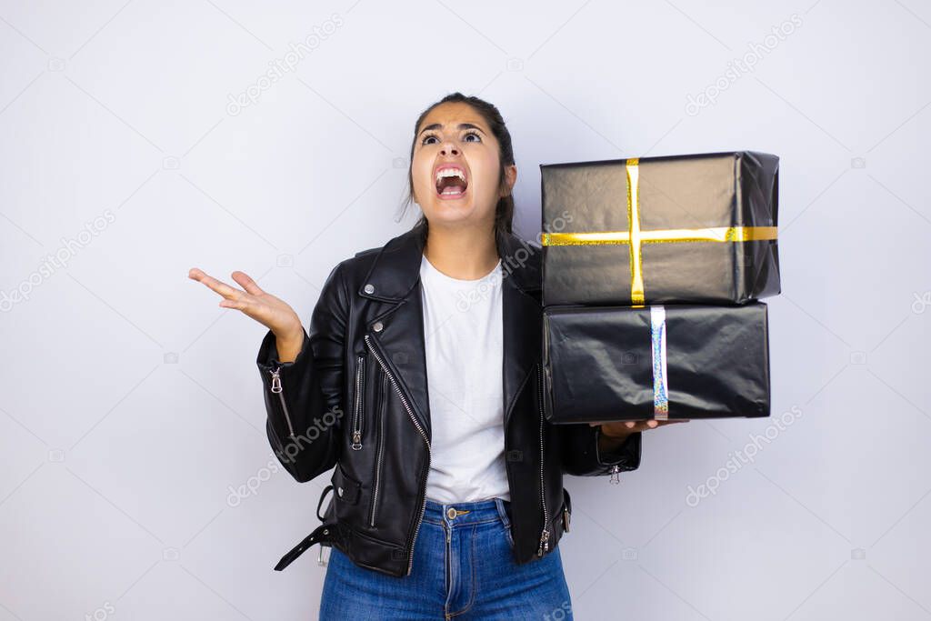 Young beautiful woman holding gifts over isolated white background crazy and mad shouting and yelling with aggressive expression and arms raised