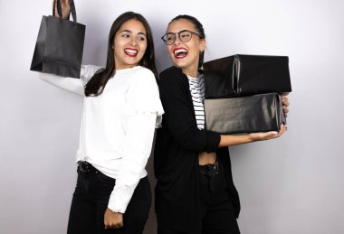 Siyah alışveriş torbaları ve kutular taşıyan iki güzel kadın birbirlerine gülümsüyor. Kara Cuma