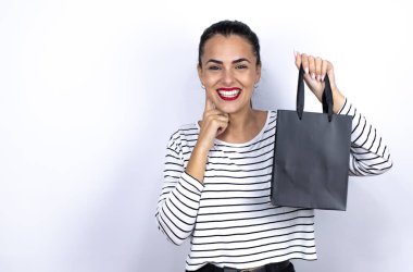 Siyah bir alışveriş çantası tutan genç ve güzel bir kadın gülümsüyor ve parmaklarını ve ağzını gösterip işaret ediyor. Kara Cuma