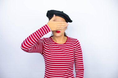 Genç, güzel esmer kadın, Fransız beresi takıyor ve beyaz arka planda gözlük takıyor. Ciddi ve elleriyle gözlerini kapatıyor.