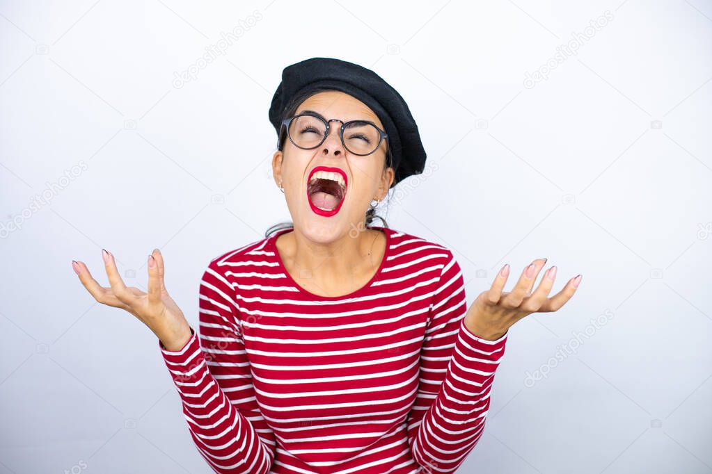 Young beautiful brunette woman wearing french beret and glasses over white background clueless and confused expression with arms and hands raised