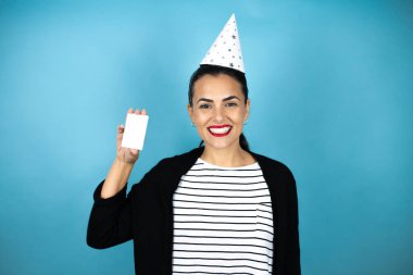 Doğum günü şapkası takan, mavi arka planda gülümseyen ve elinde beyaz kart tutan güzel bir kadın.