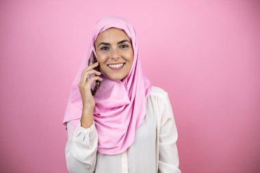 Genç, güzel bir Arap kadın, soyutlanmış pembe arka planda tesettür takıyor. Telefonu at.