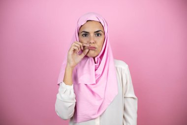 Genç, güzel bir Arap kadın, izole edilmiş pembe arka plan ağzı ve dudakları parmaklarıyla kapanmış fermuar gibi olan İslami başörtüsü takıyor. Gizli ve sessiz, tabu konuşması