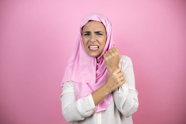 Genç, güzel bir Arap kadın, izole edilmiş pembe arka plan üzerine tesettür takıyor. Ellerinde ve parmaklarında ağrı, iltihaplanma.