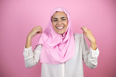 Genç, güzel bir Arap kadın, izole edilmiş pembe bir arkaplanda başarılı bir ifadeyle İslami başörtüsü takıyor.