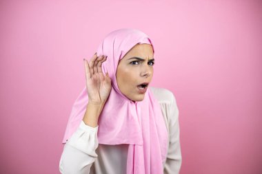 İzole edilmiş pembe arka plan üzerinde İslami başörtüsü takan genç, güzel bir Arap kadın kulağına gelen dedikoduları ve dedikoduları duyunca şaşırdı.