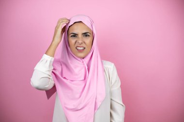Genç, güzel bir Arap kadın soyutlanmış pembe arka plan karışıklığı üzerine İslami başörtüsü takıyor ve soru soruyor. Şüpheyle karışık, kafa kafaya düşünerek.