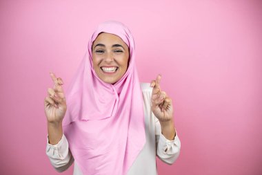 Genç, güzel bir Arap kadın, izole edilmiş pembe arka plan üzerine başörtüsü takıyor. Umut ve bakışlarla gülümsüyor.