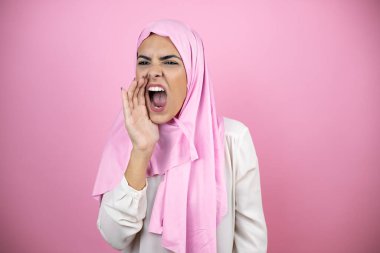 Genç, güzel bir Arap kadın, izole edilmiş pembe arka planda İslami başörtüsü takıyor. Ağızdan ağıza yüksek sesle bağırıyor ve çığlık atıyor.