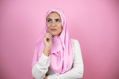 Genç, güzel bir Arap kadın, soyutlanmış pembe arka plan üzerinde İslami başörtüsü takıyor. Düşünüyor ve yan tarafa bakıyor.