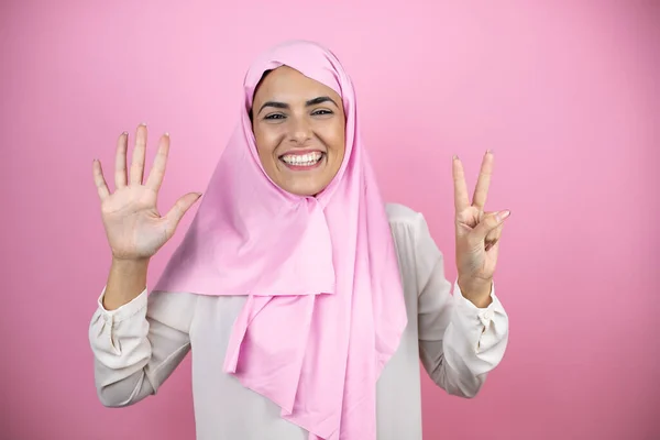 若いです美しいですArab女性身に着けていますイスラムヒジャーブ上の隔離されたピンクの背景ショーと指しています指数7とともに笑顔自信と幸せ — ストック写真