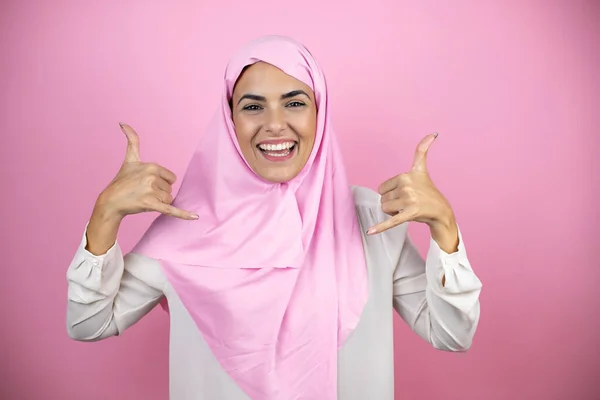 若いです美しいですArab女性身に着けていますイスラムヒジャーブ上の隔離されたピンクの背景叫びますとともにクレイジー式行うロックシンボルとともに手アップ — ストック写真
