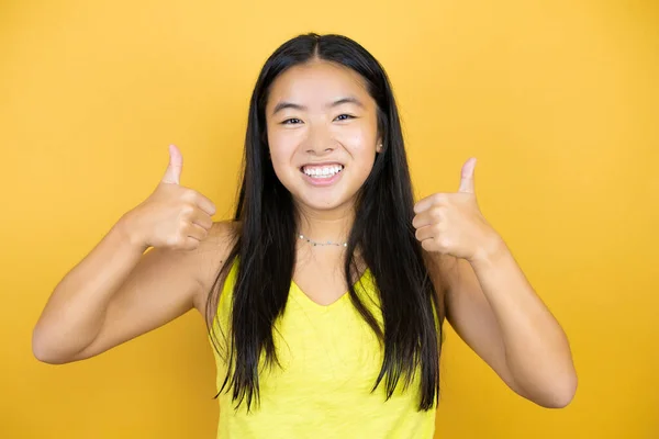 年轻美丽的亚洲女人在黄色孤立的背景下成功地做着手势 用手做着积极的手势 竖起大拇指微笑着 快乐地 快乐的表情和胜利的姿态 — 图库照片