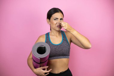 İzole edilmiş pembe arka planda spor kıyafetleri giyen genç bir kadın pis ve iğrenç bir koku alıyor. Dayanılmaz bir koku. Nefesini burnunda tutuyor..