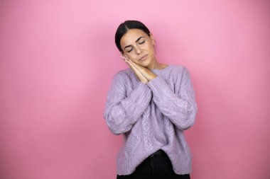 Güzel bir kadın pembe arka planda sıradan bir mor kazak giyer uyur, yorgun düşler kurar ve elleriyle poz verir, gözleri kapalı gülümserdi..